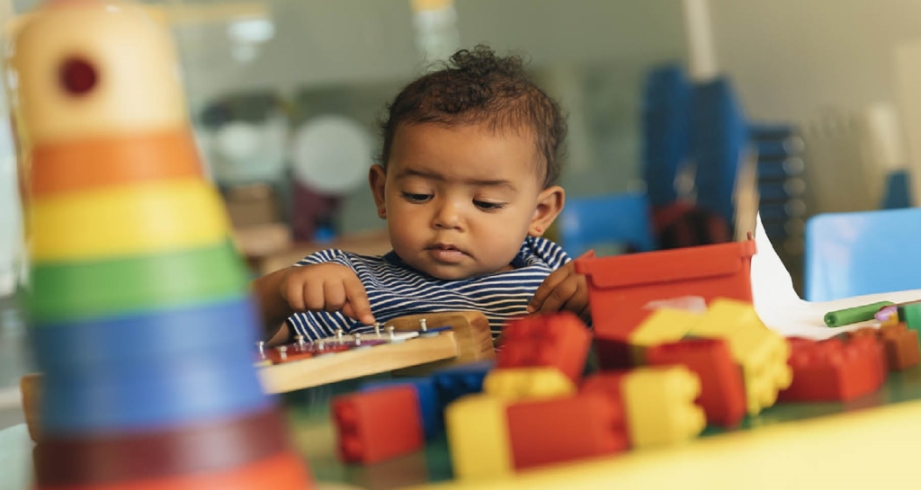 Toddler playing with colorful building blocks and a wooden activity board.