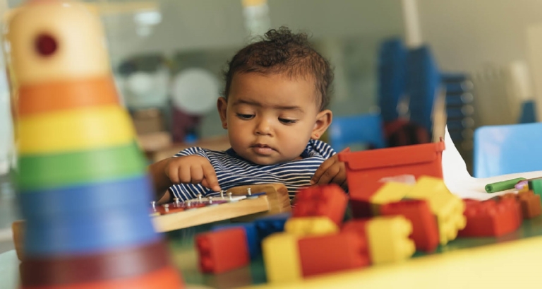 Toddler playing with colorful building blocks and a wooden activity board.