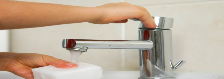 Hand turning on water from a faucet.