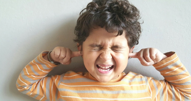 Boy in striped shirt covering his ears and squeezing his eyes shut.
