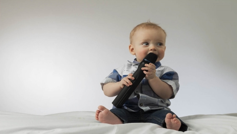 A baby sitting on a bed holding a TV remote control.
