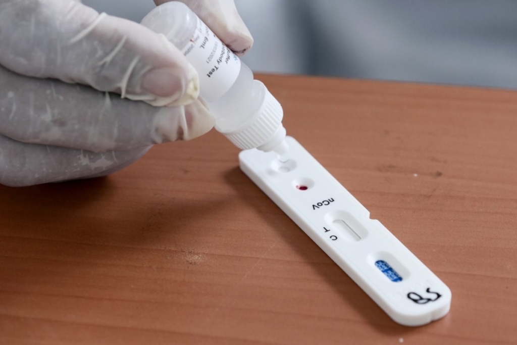 Gloved hand applying liquid to a COVID-19 rapid test kit.