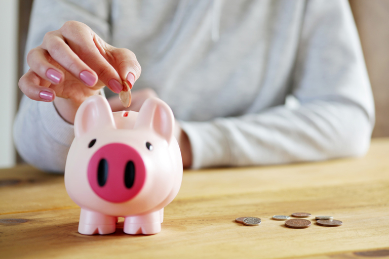 Hand placing a coin into a pink piggy bank.