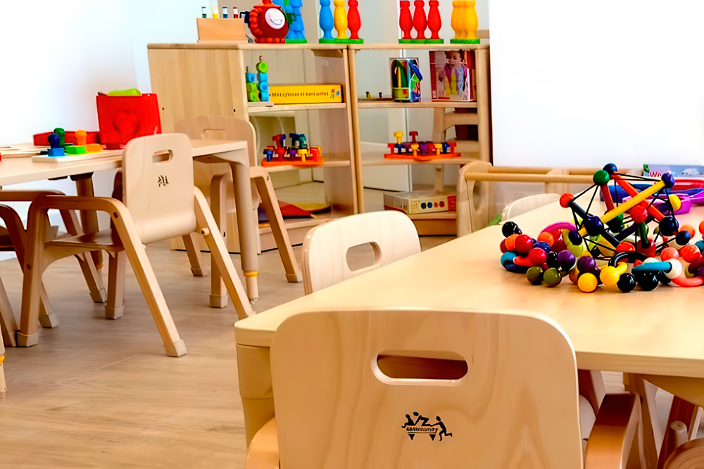Colorful preschool classroom with wooden tables, chairs, and educational toys neatly arranged.