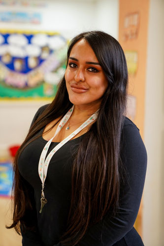 Woman smiling while wearing a lanyard in a classroom.