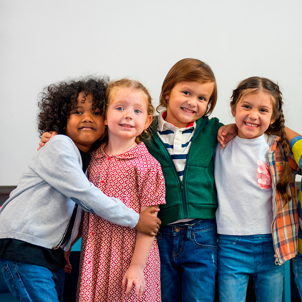 Four young children standing close, smiling warmly, and hugging each other in friendship.