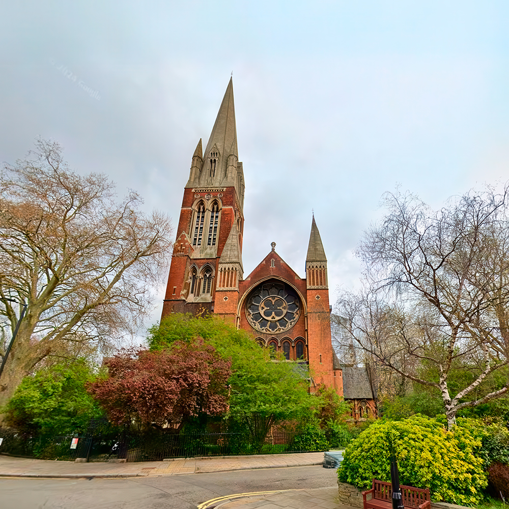 Red brick church with tall spire surrounded by trees.