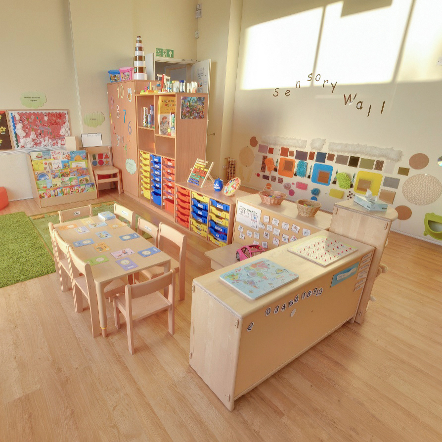 Colorful classroom with tables, chairs, and a sensory wall.