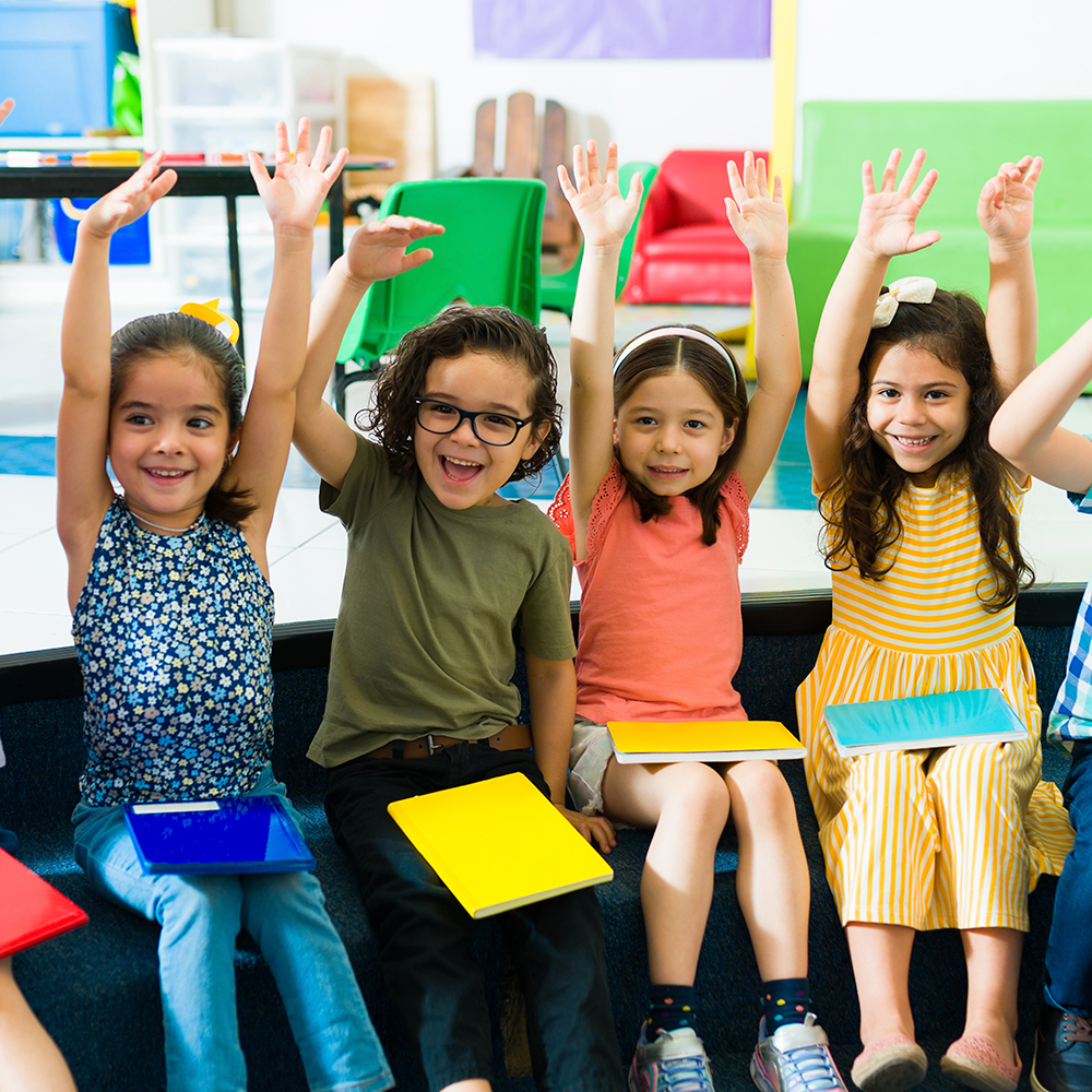 Four smiling kids raising hands with colorful folders.