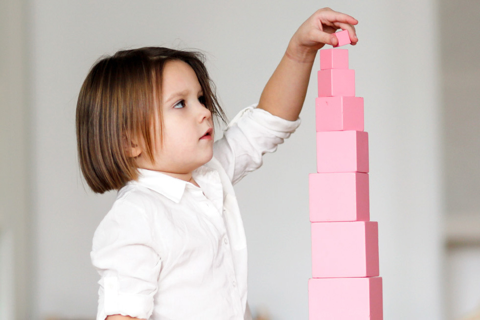 Child stacking pink blocks with focus and precision.