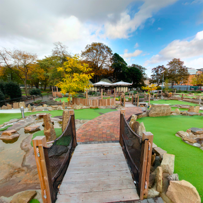 Outdoor mini-golf course with wooden bridge and green turf.